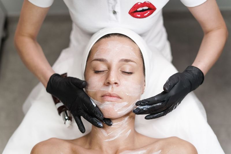 An esthetician applying a treatment mask to a client resting on a treatment bed