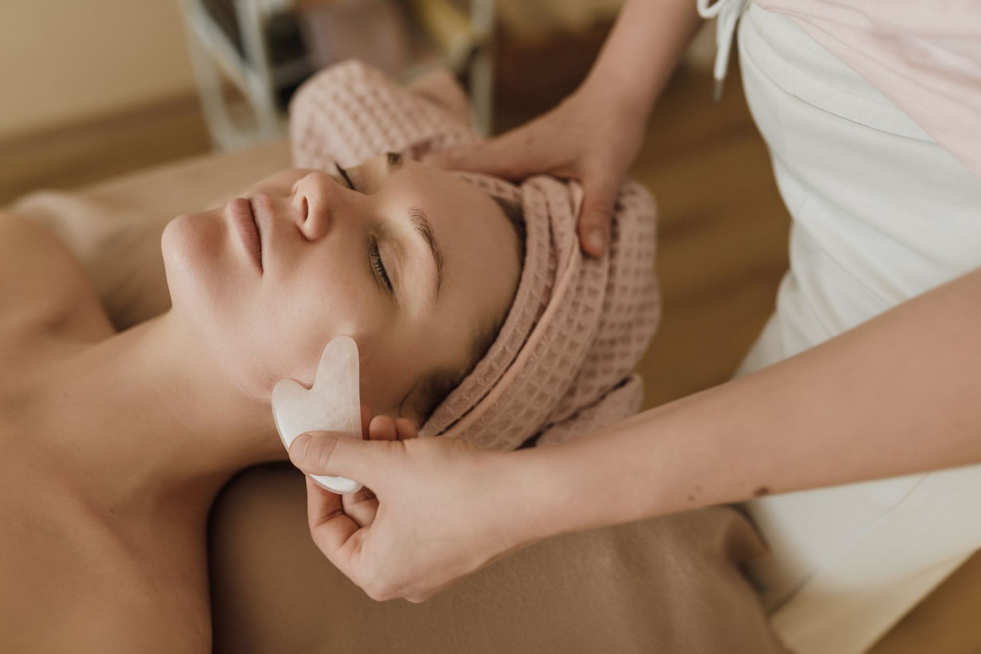 An esthetician performing a contouring facial treatment on a client resting in a warm, softly lit treatment room