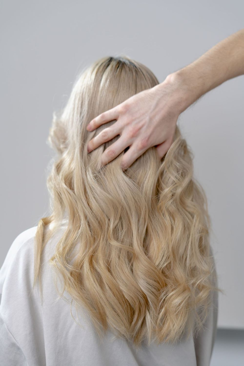 A stylist's hand resting on a client's long, softly waved blonde hair after styling